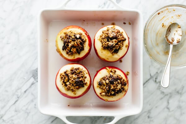 Four apples stuffed with filling in a baking dish.