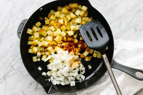 Diced potatoes, onions, and seasonings in a skillet for breakfast potatoes.