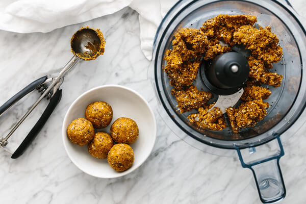 Blended mango energy balls in a food processor next to a bowl of them.