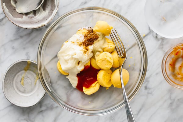 Filling ingredients for spicy deviled eggs in a bowl with a fork.