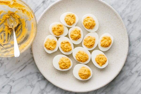 Spicy deviled eggs on a plat next to a bowl of yolk filling.