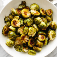 A bowl of roasted Brussels sprouts on a table next to a spoon.