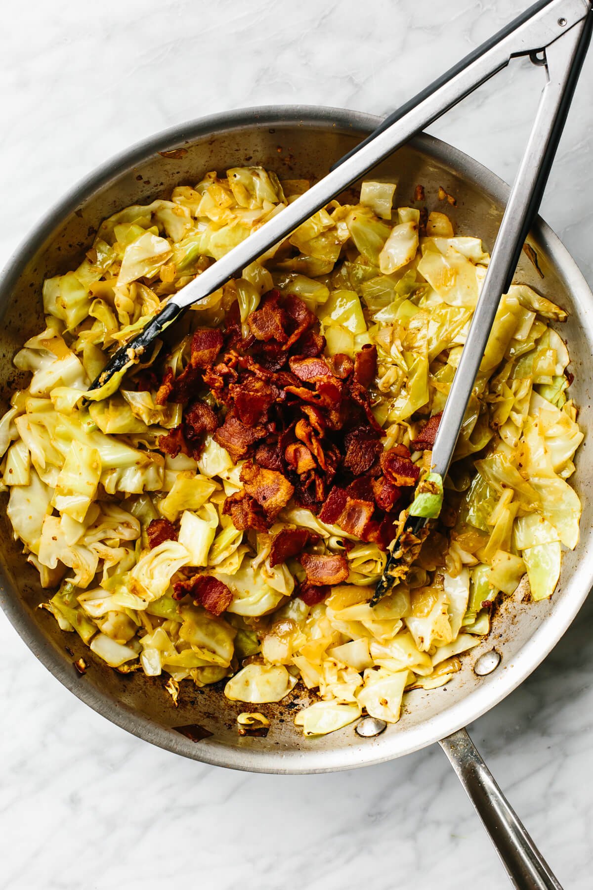 Tossing bacon into fried cabbage in a pan