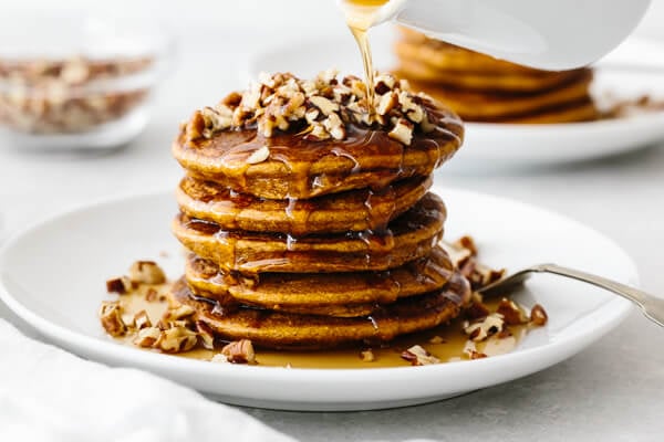 A stack of paleo pumpkin pancakes on a white plate, topped with pecans.