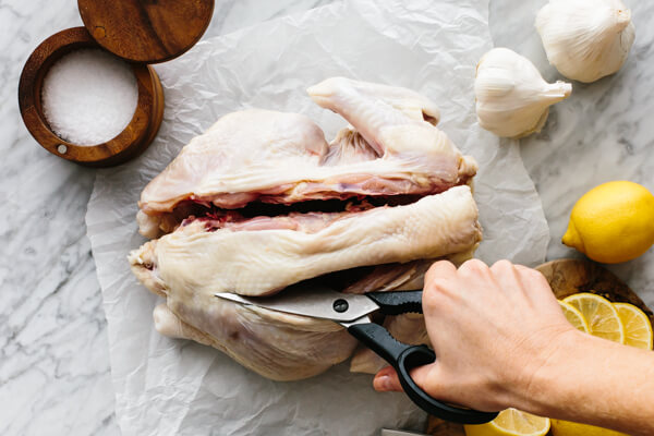 Spatchcocking a chicken by cutting down the side of backbone.
