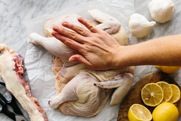 A spatchcocked chicken being flattened by hands.
