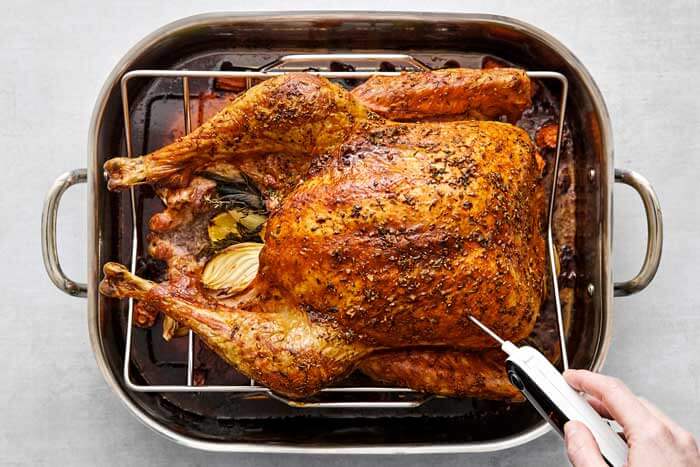 Checking the temperature of a roasted turkey in roasting pan.