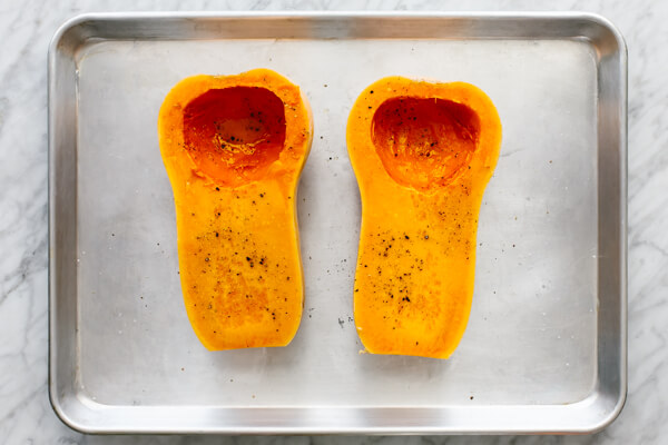 Butternut squash halves on a baking sheet for orange shakshuka.