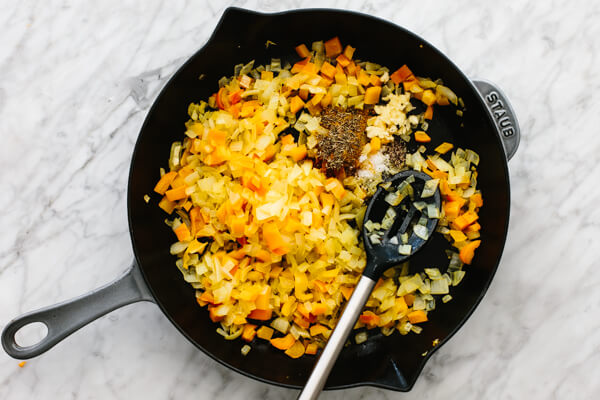 Spiced being added to an orange shakshuka mixture.