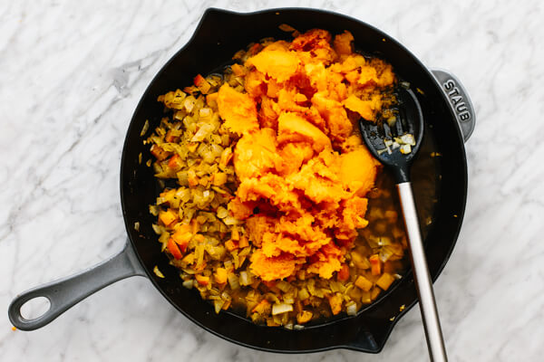 Butternut squash being added to an orange shakshuka mixture.