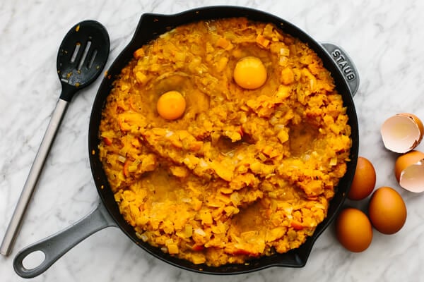 Adding eggs to an orange shakshuka in a skillet.