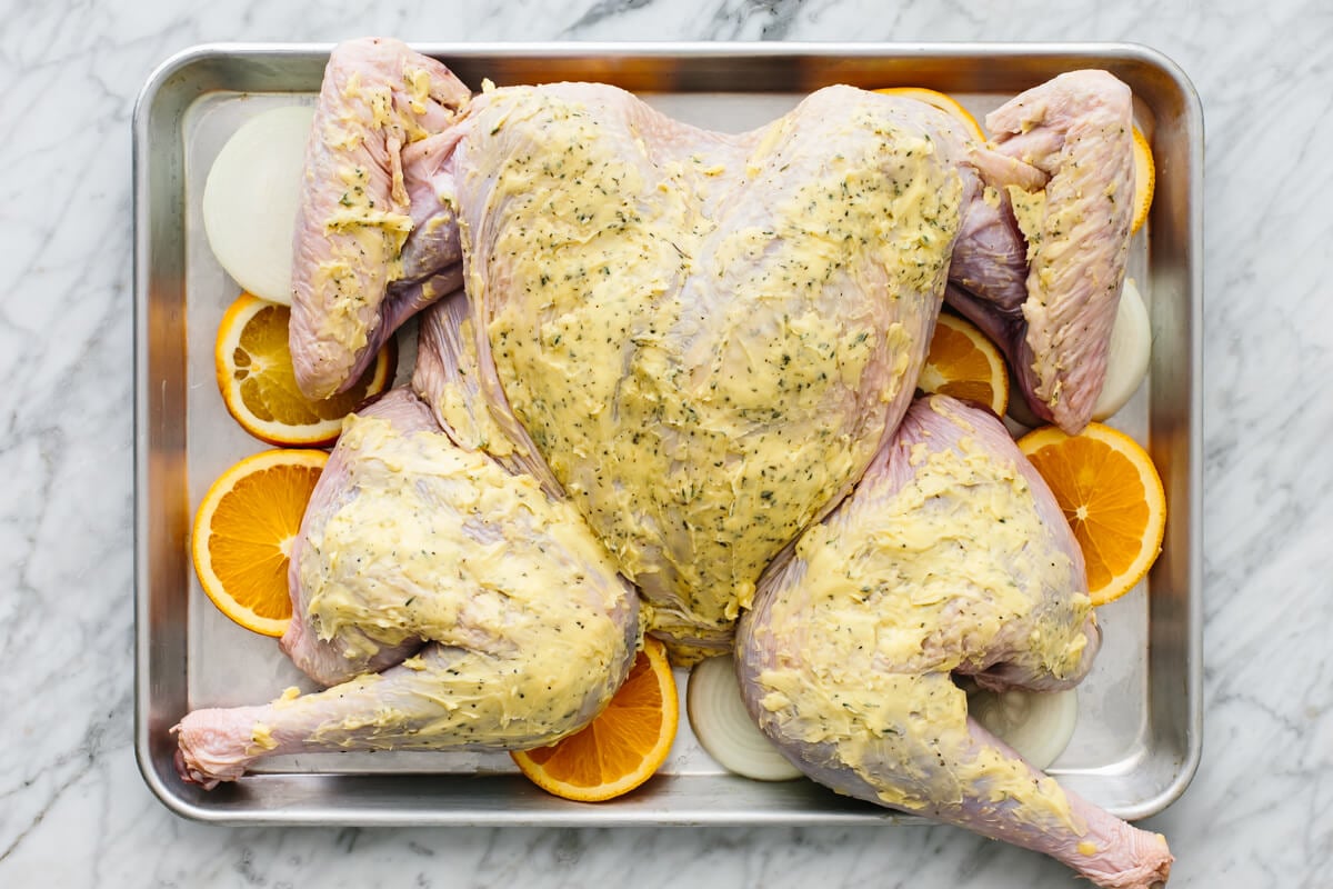Maple orange glazed spatchcock turkey on a sheet pan before baking.