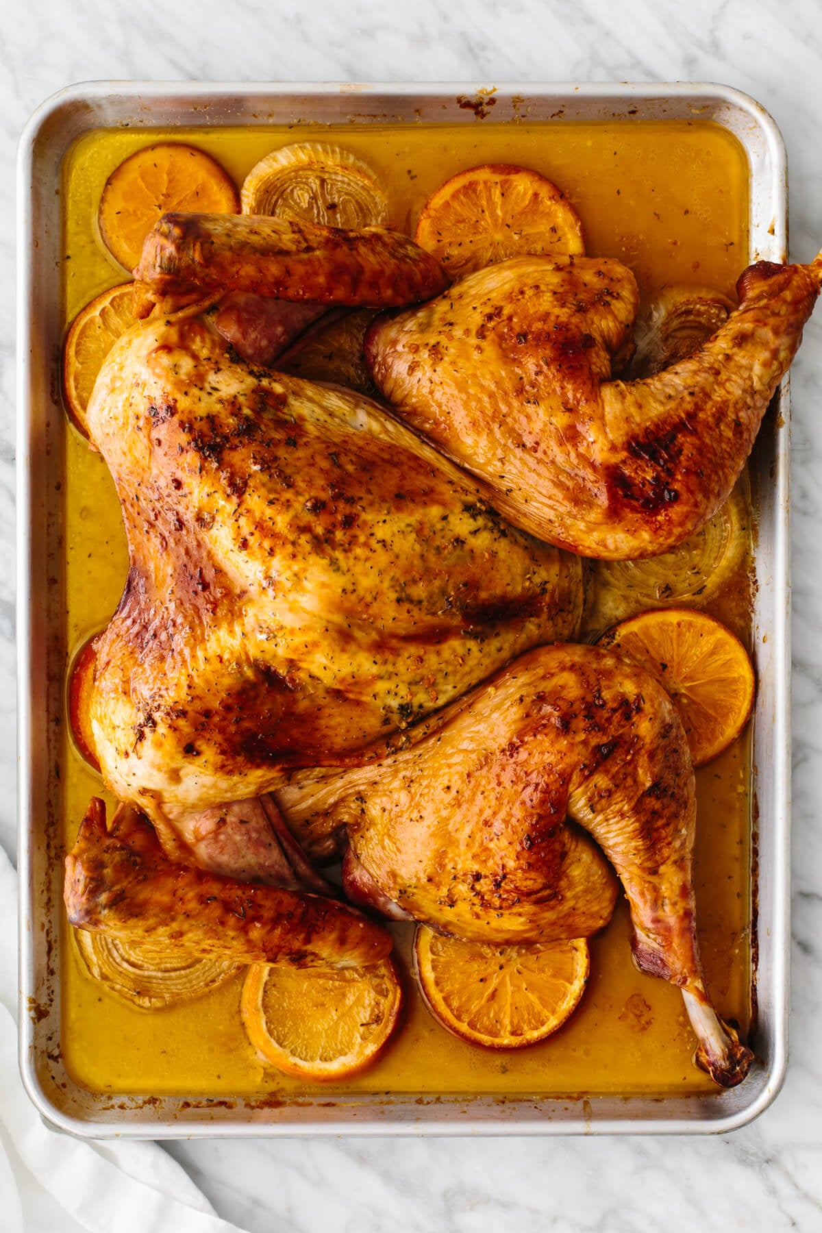 This maple orange spatchcock turkey is here to steal the Thanksgiving spotlight! It's juicy, sweet, citrusy, and perfectly crispy. A baking sheet with an orange glazed spatchcock turkey