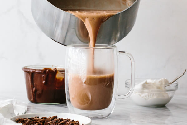 Pouring Nutella hot chocolate in a cup on a table.