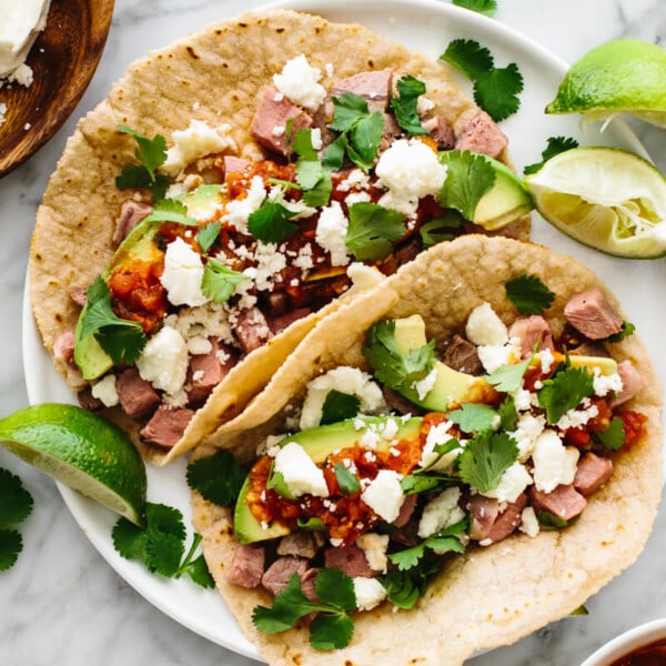 Prime rib tacos on a plate next to garnishes.