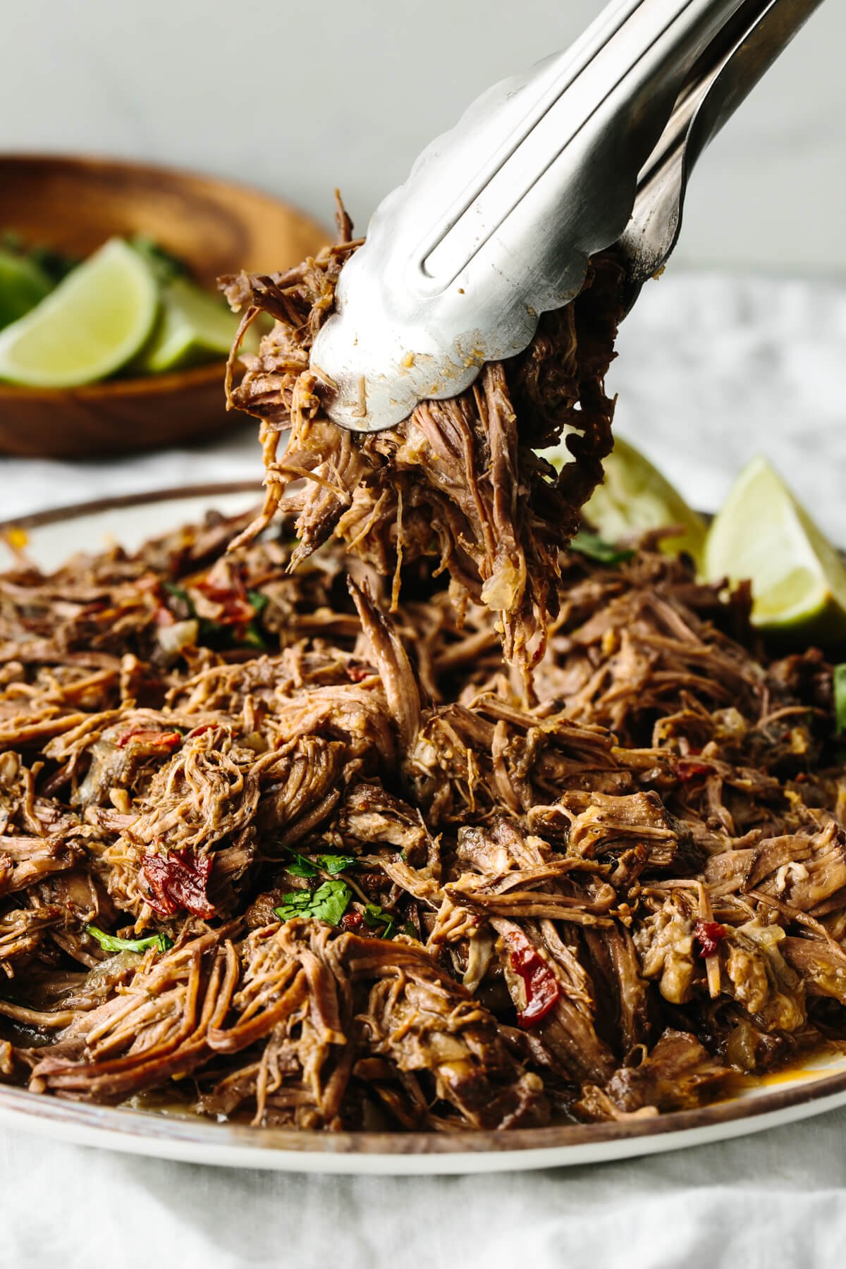 Picking up beef barbacoa from a plate with tongs.