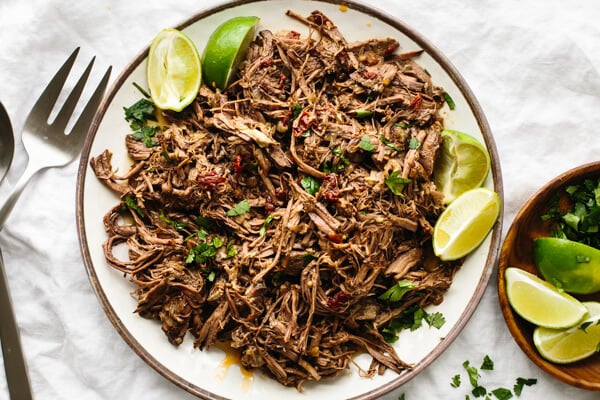 A plate of beef barbacoa and lime wedges.