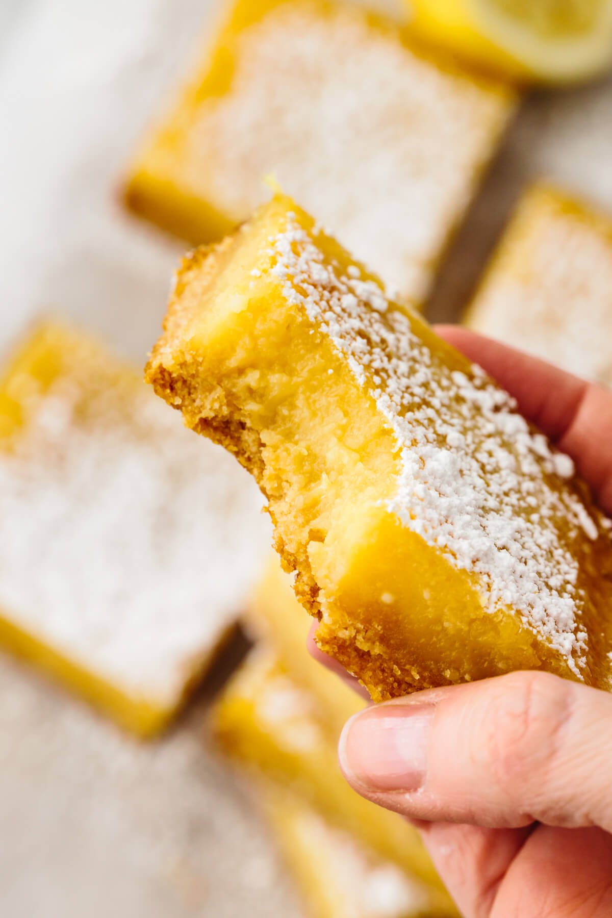 These lemon bars have a gluten-free shortbread-like crust and a bright, luscious filling that's the perfect balance of sweet and tangy! A bite out of a lemon bar.