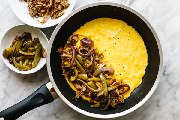 Adding carnitas to an omelette in a pan