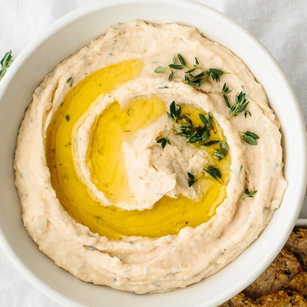 A bowl of white bean dip next to thyme and crackers.