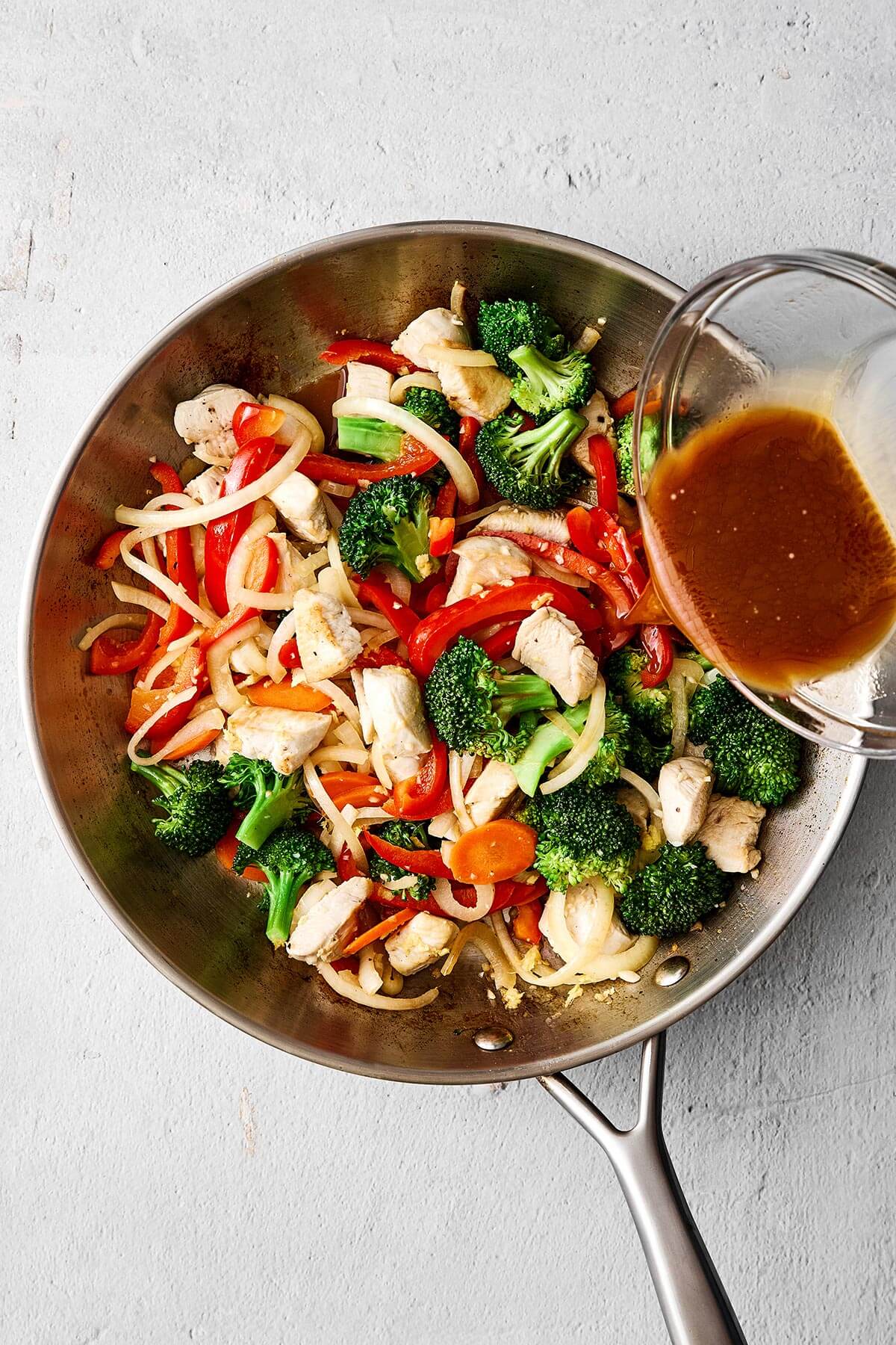 Add another splash of oil, then sauté the bell pepper, onion, carrot, and broccoli until tender, yet crisp. Cooked vegetables and chicken in a pan.