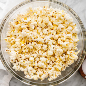 A big glass bowl of popcorn next to a napkin.