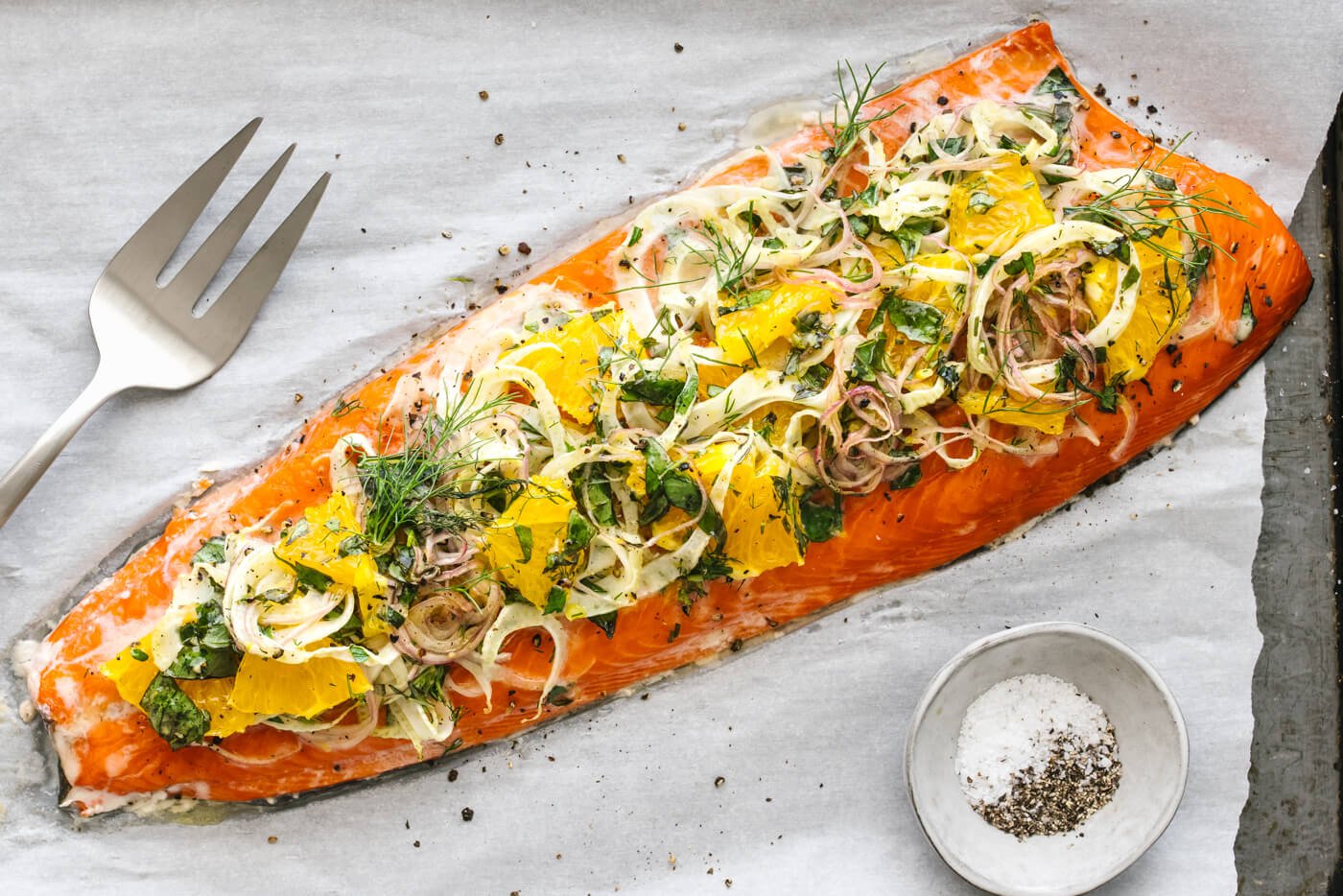 A lined baking sheet with slow roasted salmon next to a bowl of salt and pepper.