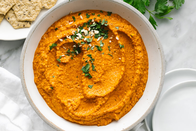 A bowl of romesco sauce next to white plates