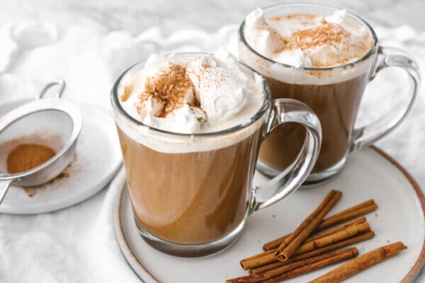 Pumpkin spice lattes next to cinnamon sticks.