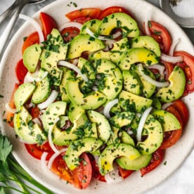 Tomato, onion, avocado salad on a plate next to a napkin