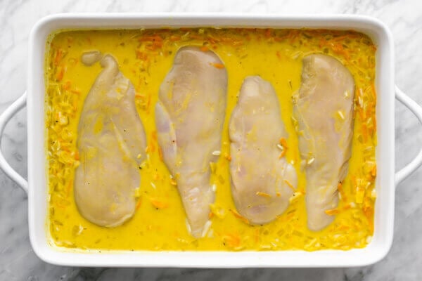 A baking dish with turmeric chicken and rice casserole ingredients.