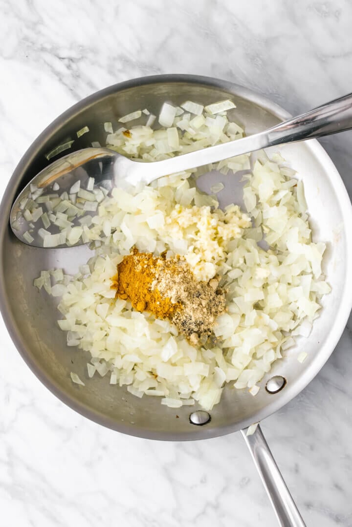 Sauteing onions and spices in a pan for turmeric chicken and rice casserole