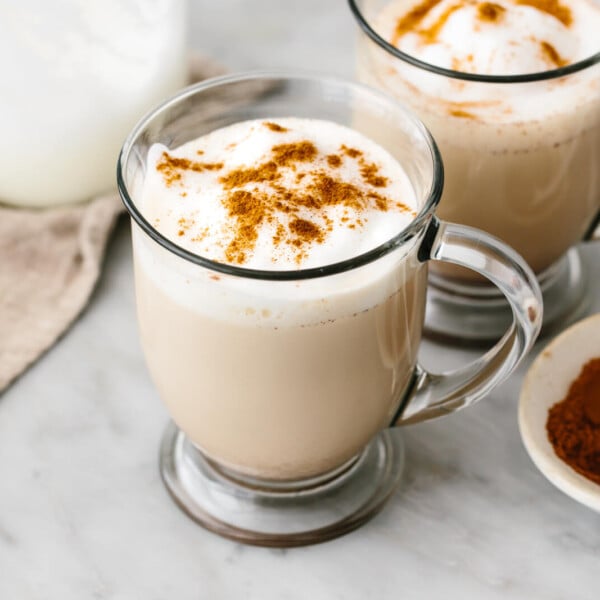 Mugs of chai latte next to a bowl of spices.