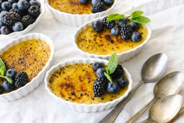 Coconut crème brûlées on a table next to berries.
