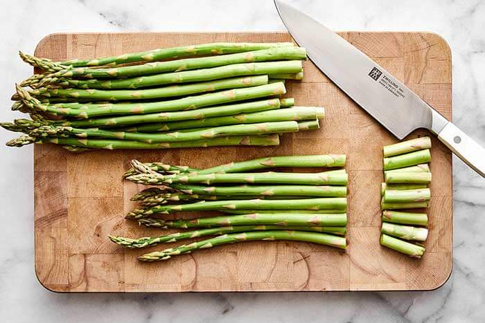 Slicing asparagus on a wooden board before roasting.