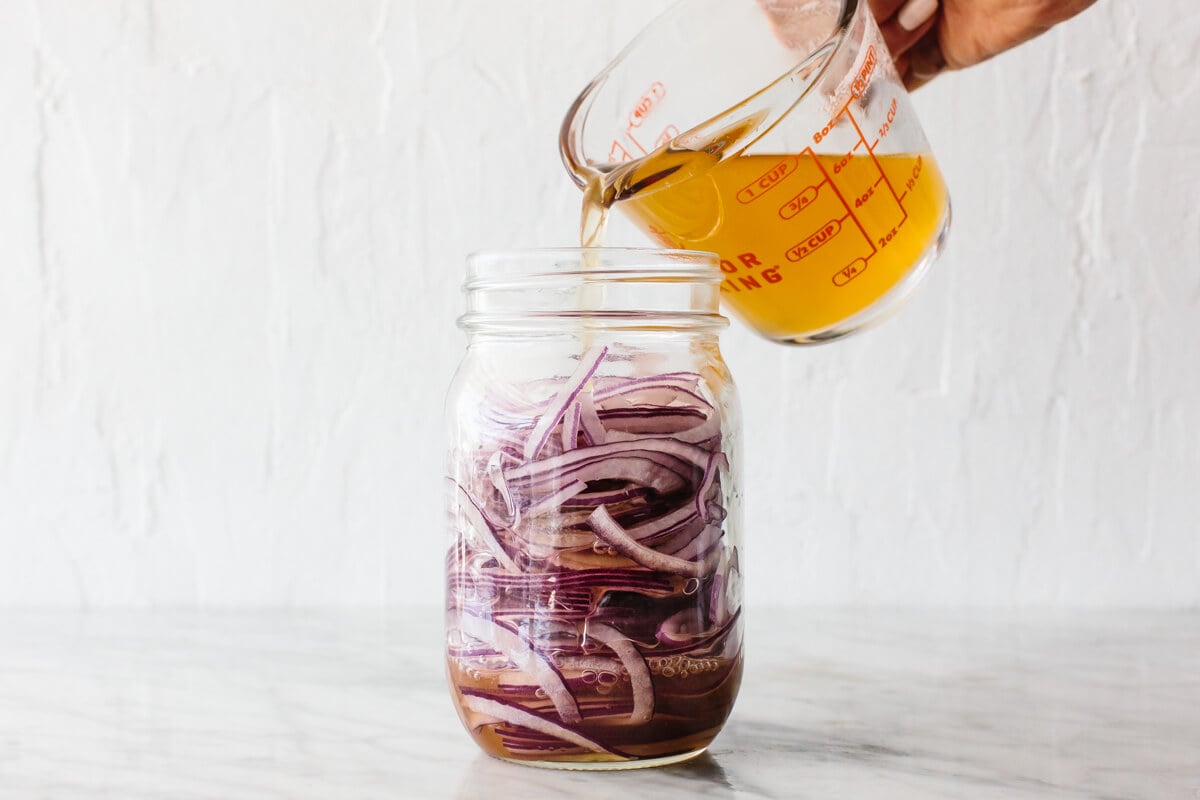 Pouring brine into a mason jar of pickled red onions