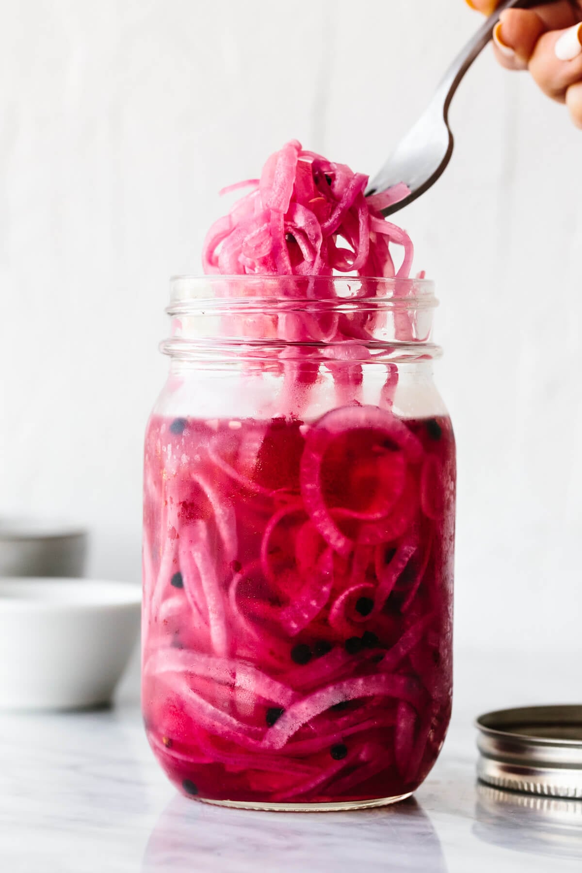 Picking up pickled red onions from a jar with a fork.