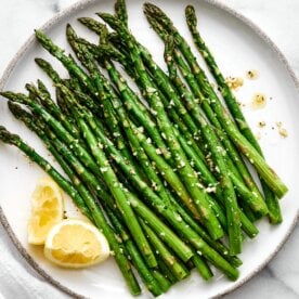 A plate of roasted asparagus with lemons.