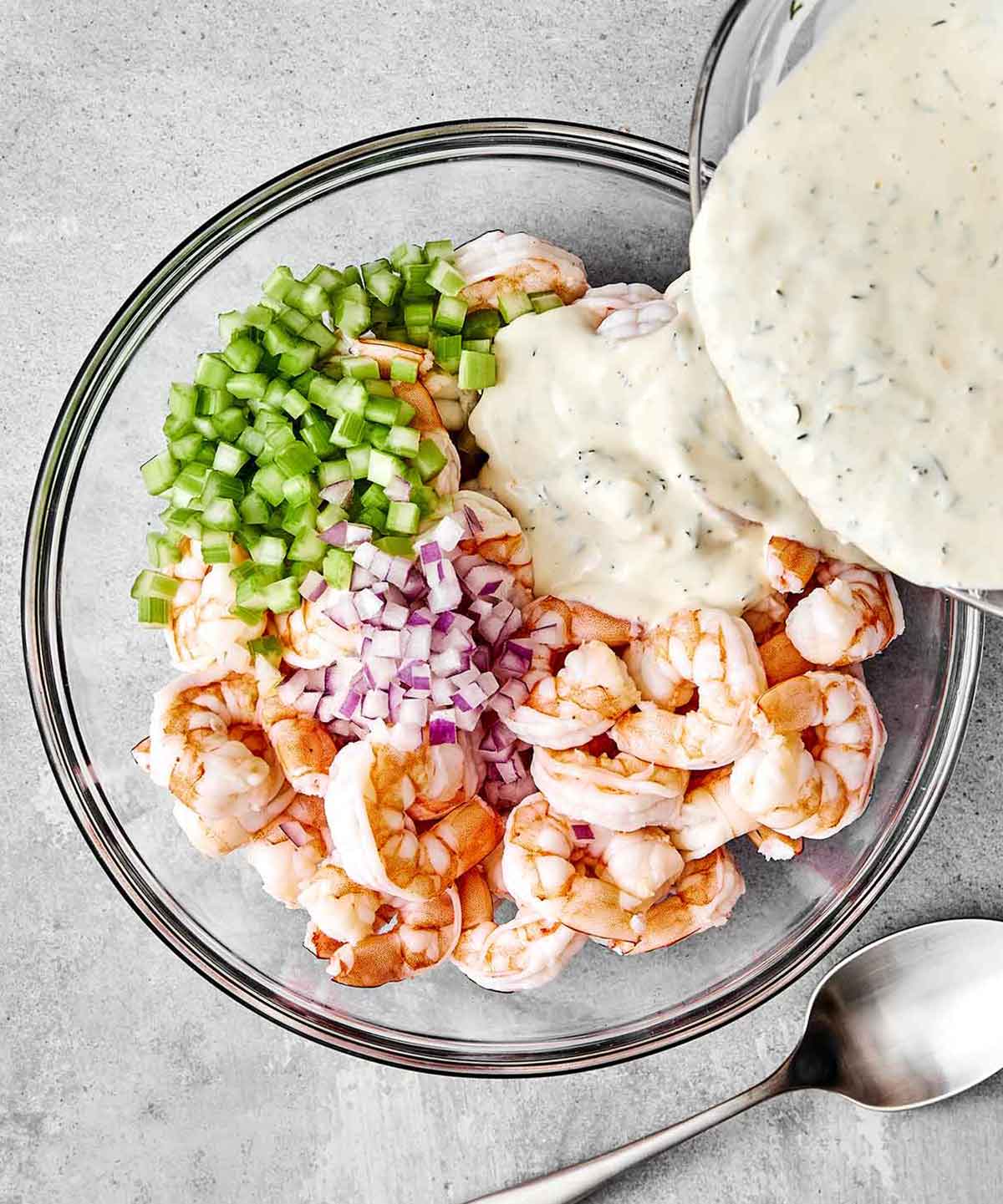 This cold shrimp salad is the ultimate summer salad! Chilled shrimp are tossed with crisp celery and red onion, then coated in a bright, creamy dressing. Adding dressing to a shrimp salad.
