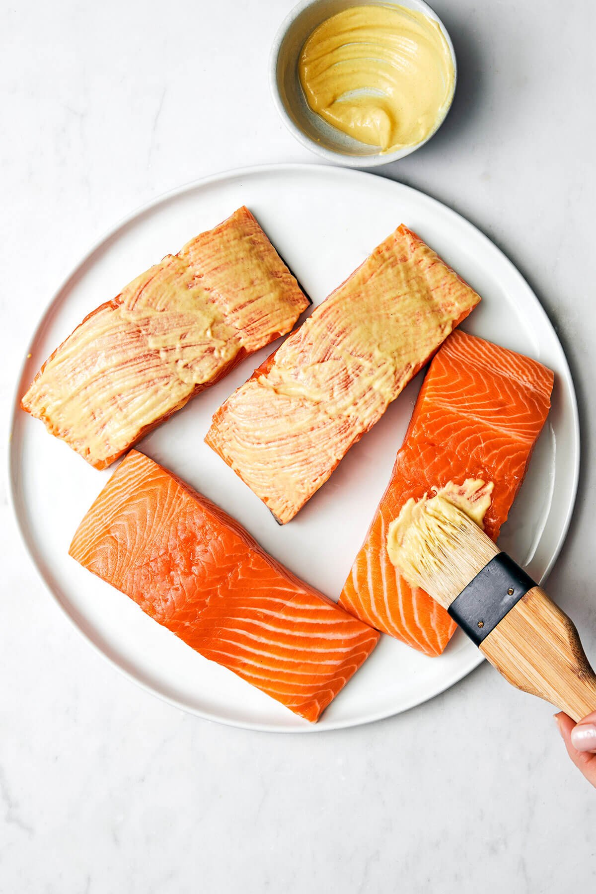 This air fryer salmon recipe is the secret to a moist and crispy filet that tastes like a million bucks - in under 15 minutes! Brushing Dijon mustard on salmon filet.