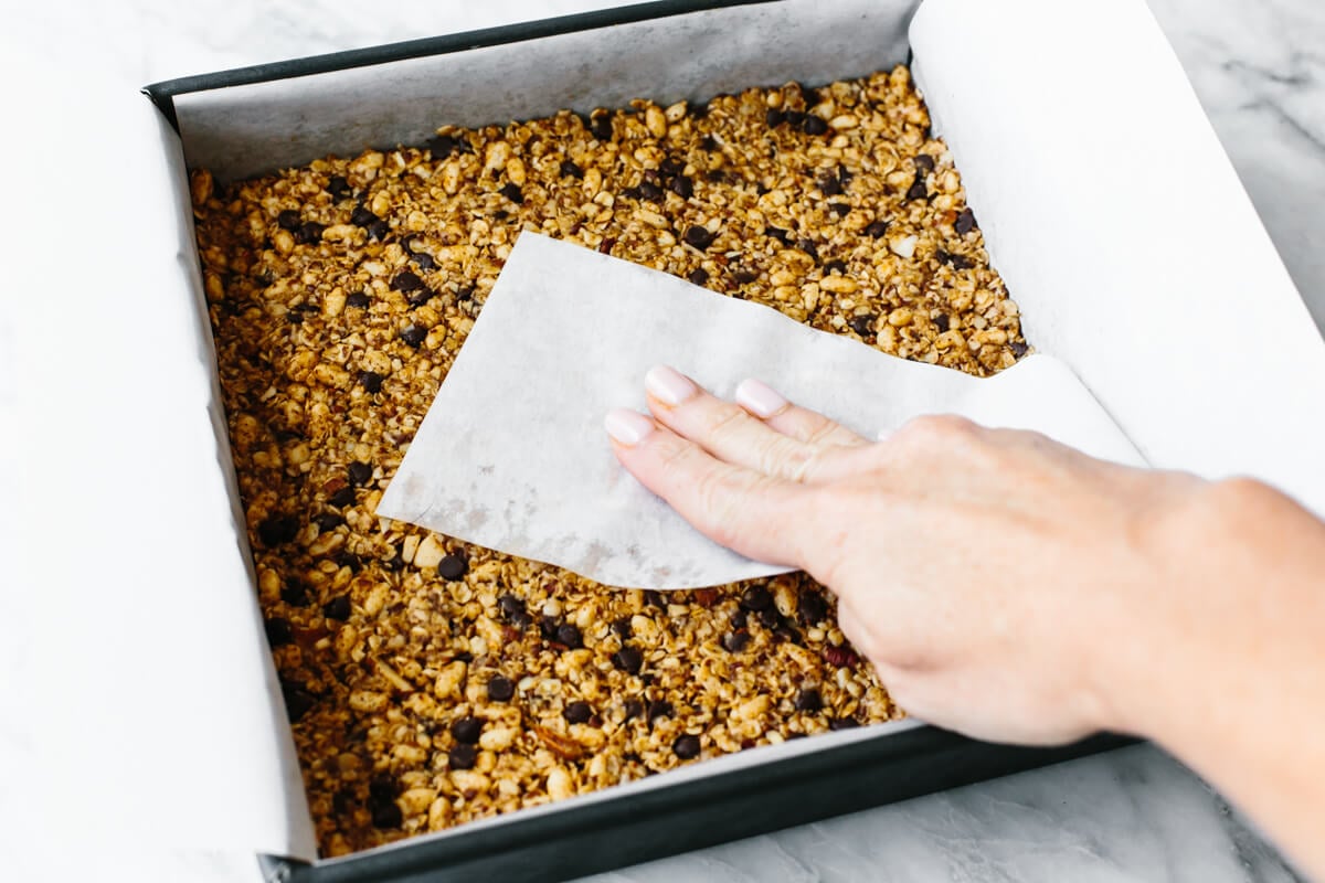 Pressing granola bar mixture into a pan with parchment paper