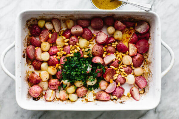 Tossing roasted radish salad ingredients in a baking dish