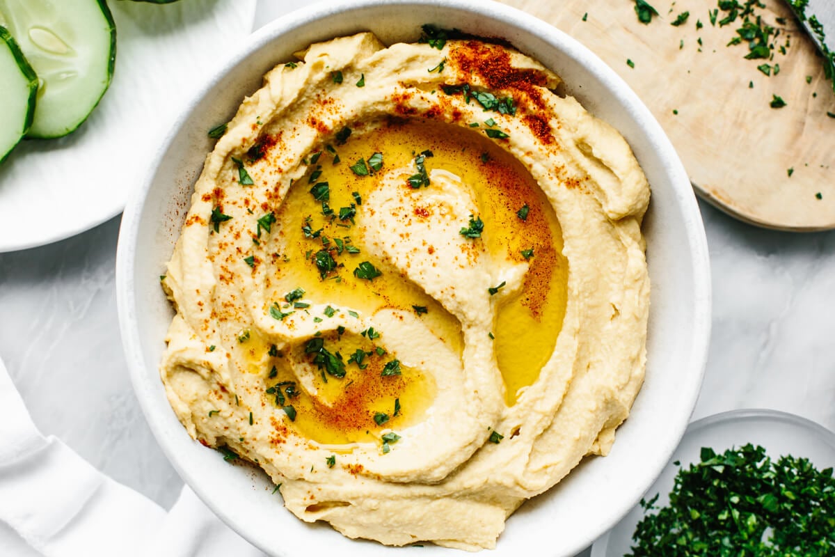 This really is the best hummus recipe! It’s a classic hummus that's creamy, savory, done in under 3 minutes with a blender. A white bowl of hummus next to chopped parsley