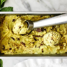 A container of mint chocolate chip nice cream next to mint leaves