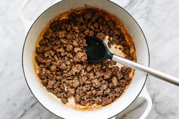 Cooking ground beef in a white pot for stuffed peppers with a spoon