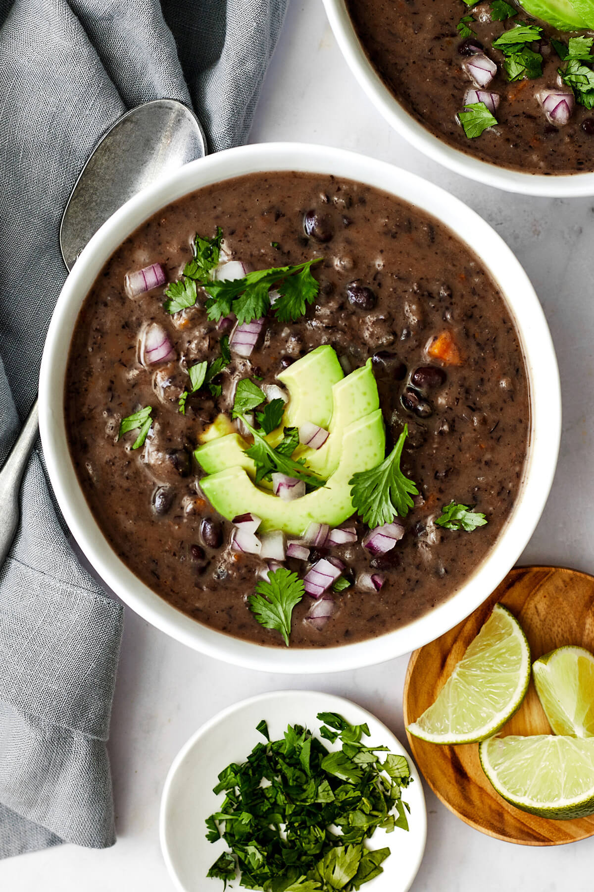 Don't look past this easy black bean soup recipe! It's a delicious vegetarian meal that's filling and layered with savory and spiced flavors. A white bowl of black bean soup next to limes