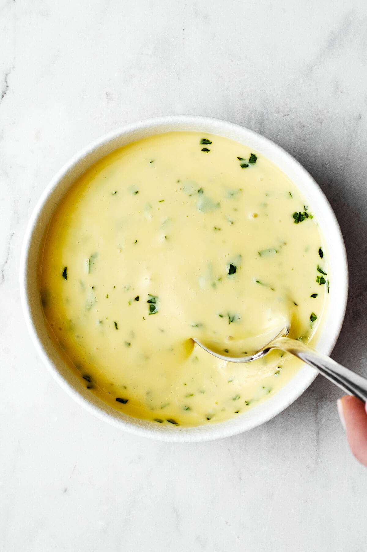 A drizzle of this easy béarnaise sauce will instantly elevate any dish! It has a luxurious butter wine base with hints of fresh tarragon. Bearnaise sauce in a white bowl with spoon