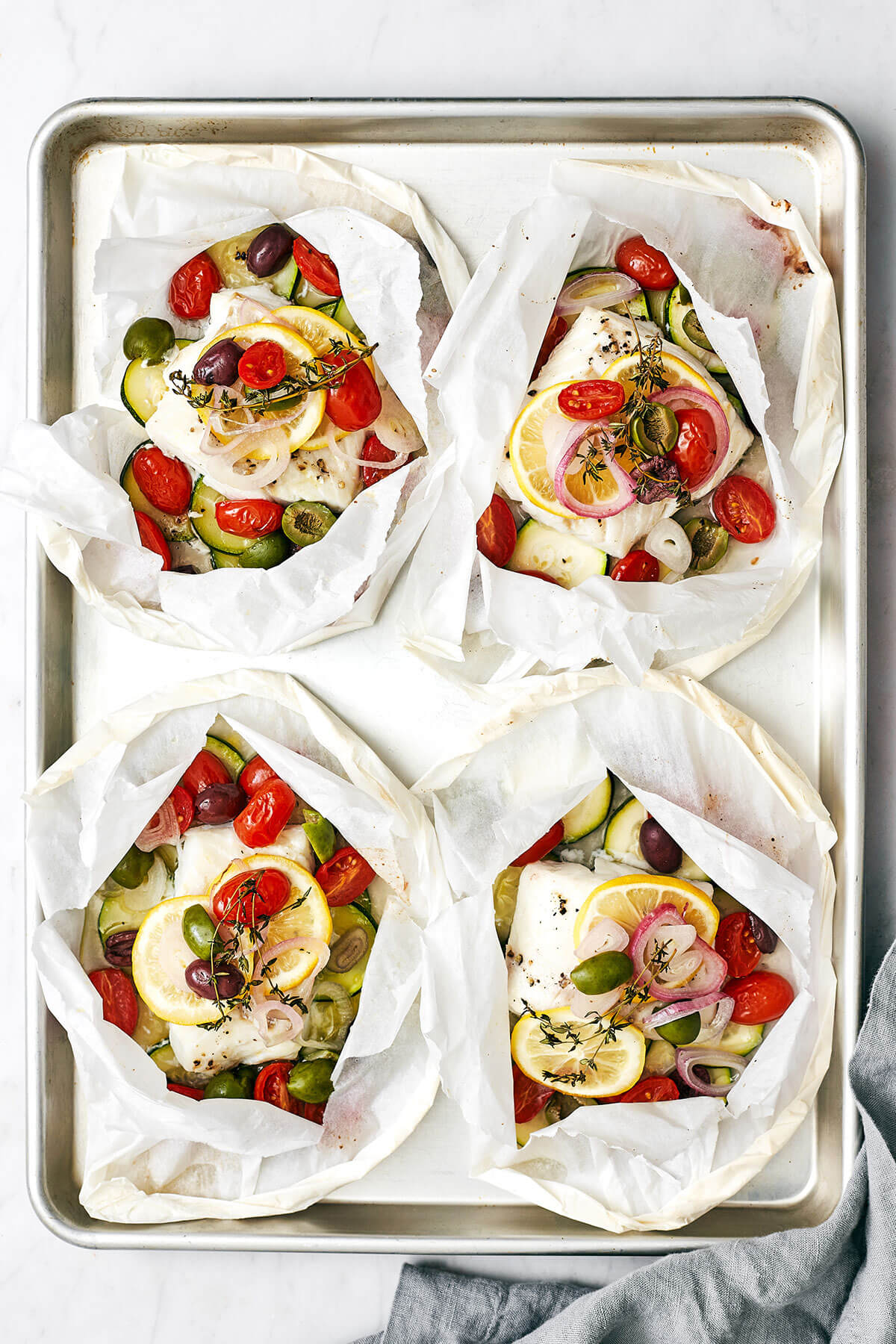 This Mediterranean cod en papillote is the most genius way to quickly achieve a simple, healthy, and super delicious dinner! Cods en papillote on a baking sheet