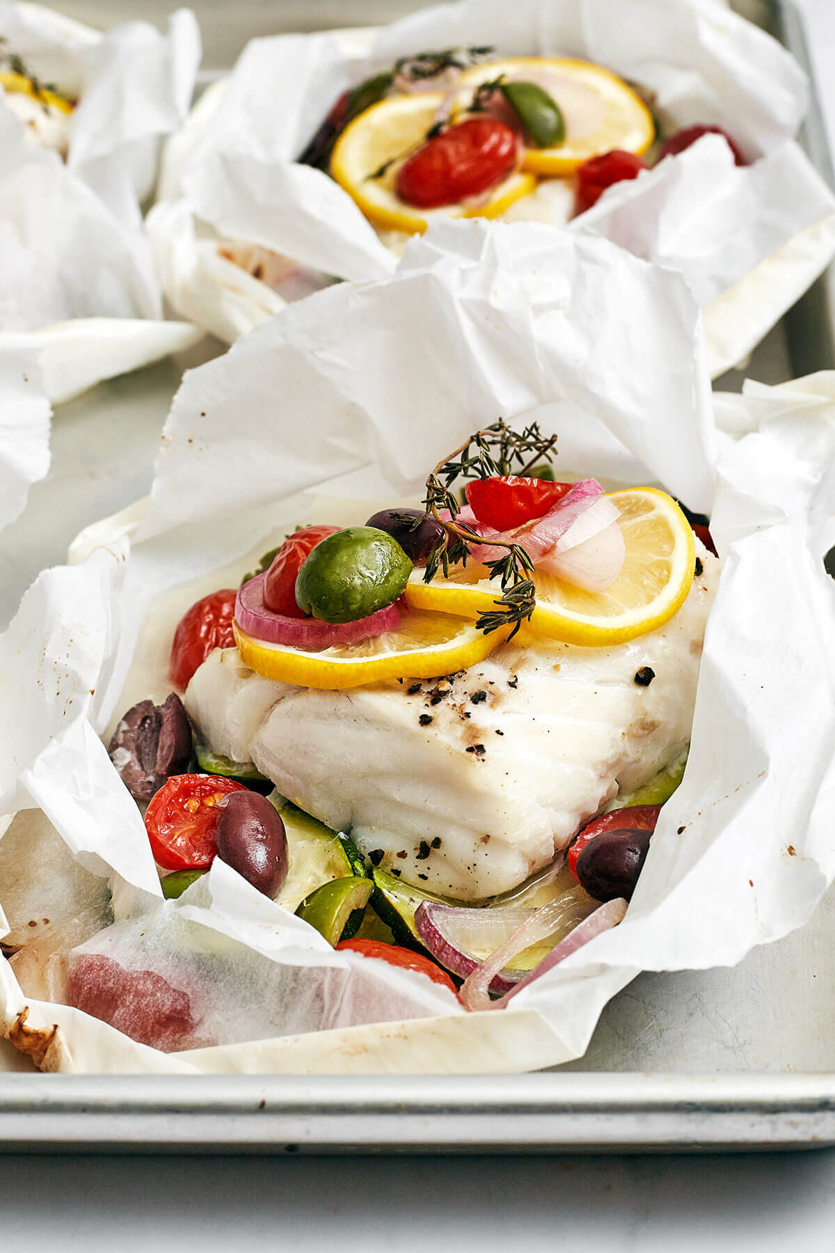 This Mediterranean cod en papillote is the most genius way to quickly achieve a simple, healthy, and super delicious dinner! Mediterranean cod en papillote on a baking sheet