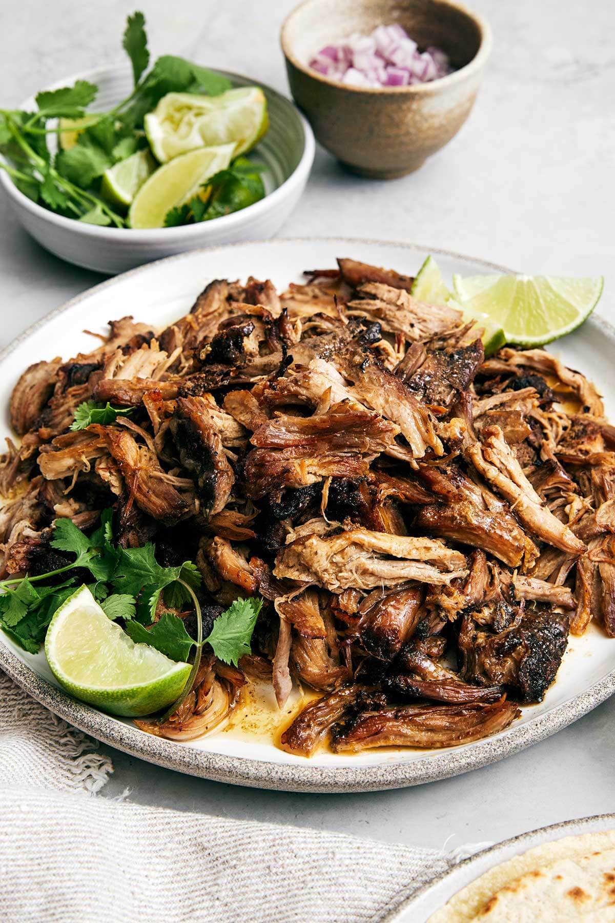 The best Mexican carnitas recipe that's juicy, full of flavor, fall-apart tender, and super easy to make in a slower cooker! A plate of carnitas with cilantro.